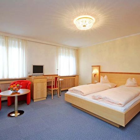 Helles Hotelzimmer mit Doppelbett, Schreibtisch, Stuhl und rotem Sessel