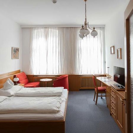 Bright hotel room with double bed, desk, television, and sitting area with red sofa