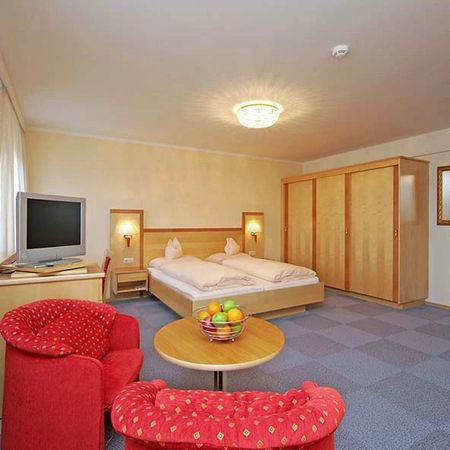 Hotel room with double bed, red sitting area, wardrobe wall, and television