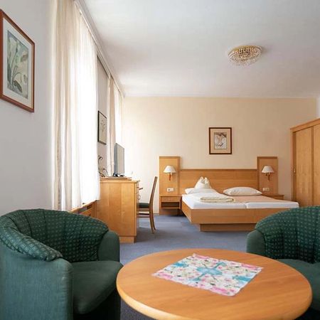 Hotel room with double bed, two green armchairs, table, and television