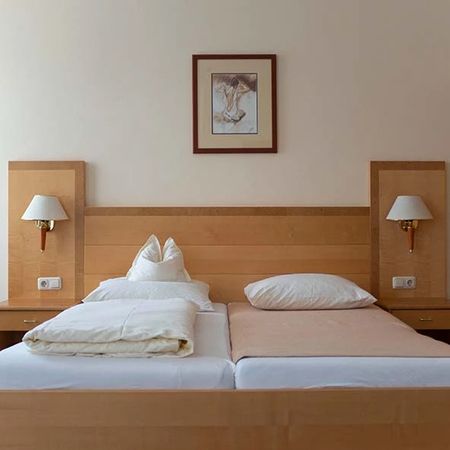 Double bed with light bed linen between two bedside tables with wall lamps