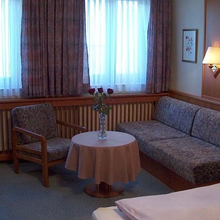 Sitting area with armchair, sofa, round table, and vase with roses in front of a window