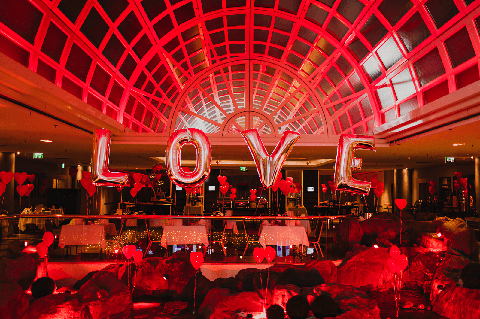 Veranstaltungsort der in rotes Licht getaucht ist mit einer großen LOVE-Ballonschrift und kleinen Herzballons