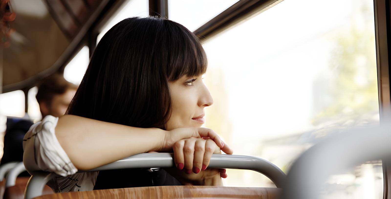 Junge Frau mit dunklen Haaren schaut aus dem Fenster eines Busses.