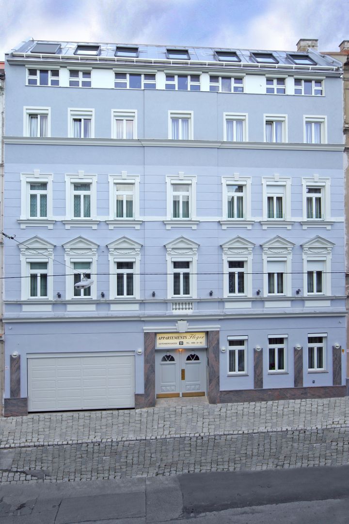 Fassade eines mehrstöckigen hellblauen Gebäudes mit weißen Fensterrahmen und Eingangstür
