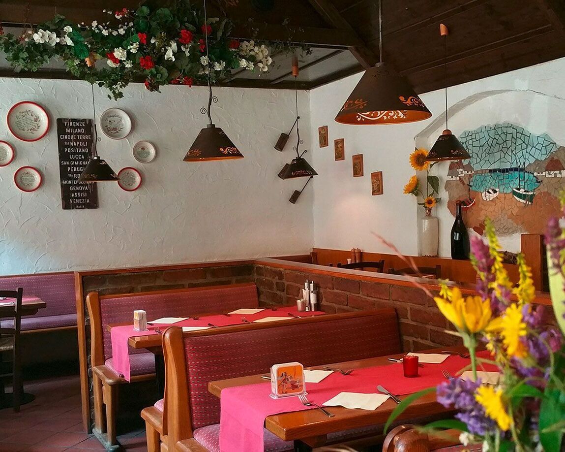 Sitzbereich eines Restaurants mit Holztischen roten Tischdecken roten Sitzbänken und weißen Wänden mit einer Wandmalerei