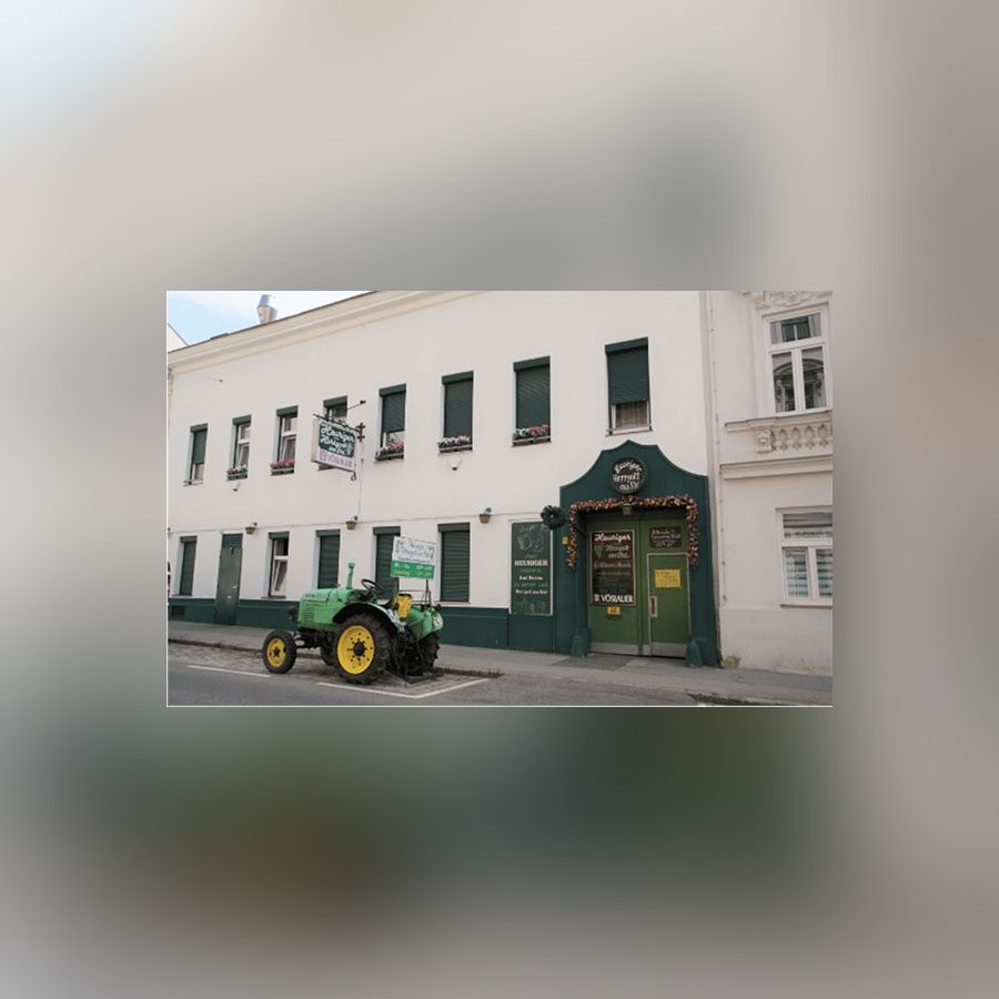 Fassade eines Heurigen mit grünem Eingangstor Fenstern und einem Traktor davor