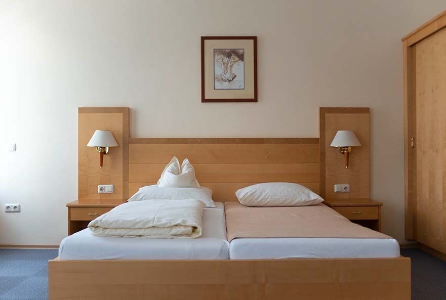 Simple bedroom with two single beds, wooden frames, bedside tables and a framed picture on the wall.