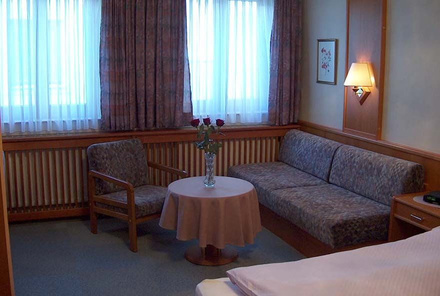 Cozy seating area with upholstered sofa, armchair, round table and vase with red roses in front of a window.