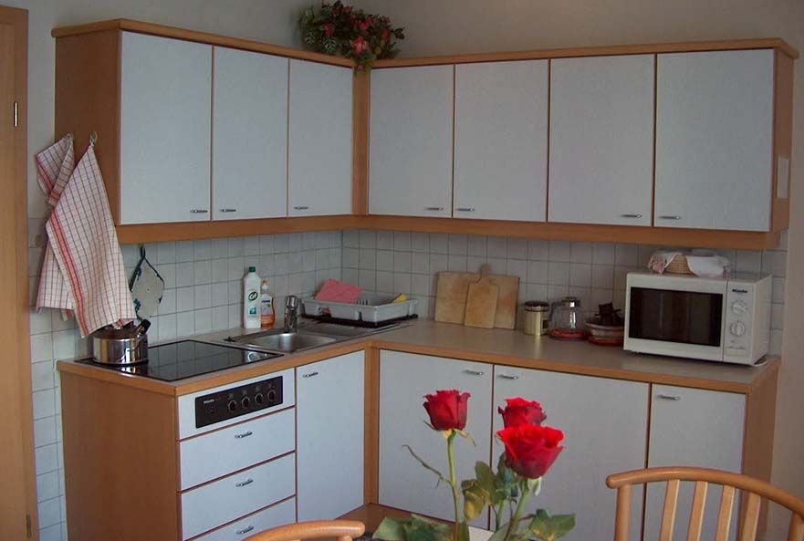 Compact fitted kitchen with white fronts, ceramic hob, microwave and fresh red roses on the table.