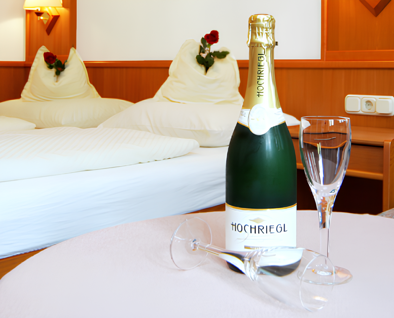 Hotel room with double bed, bottle of Hochriegl sparkling wine, and two glasses on a table