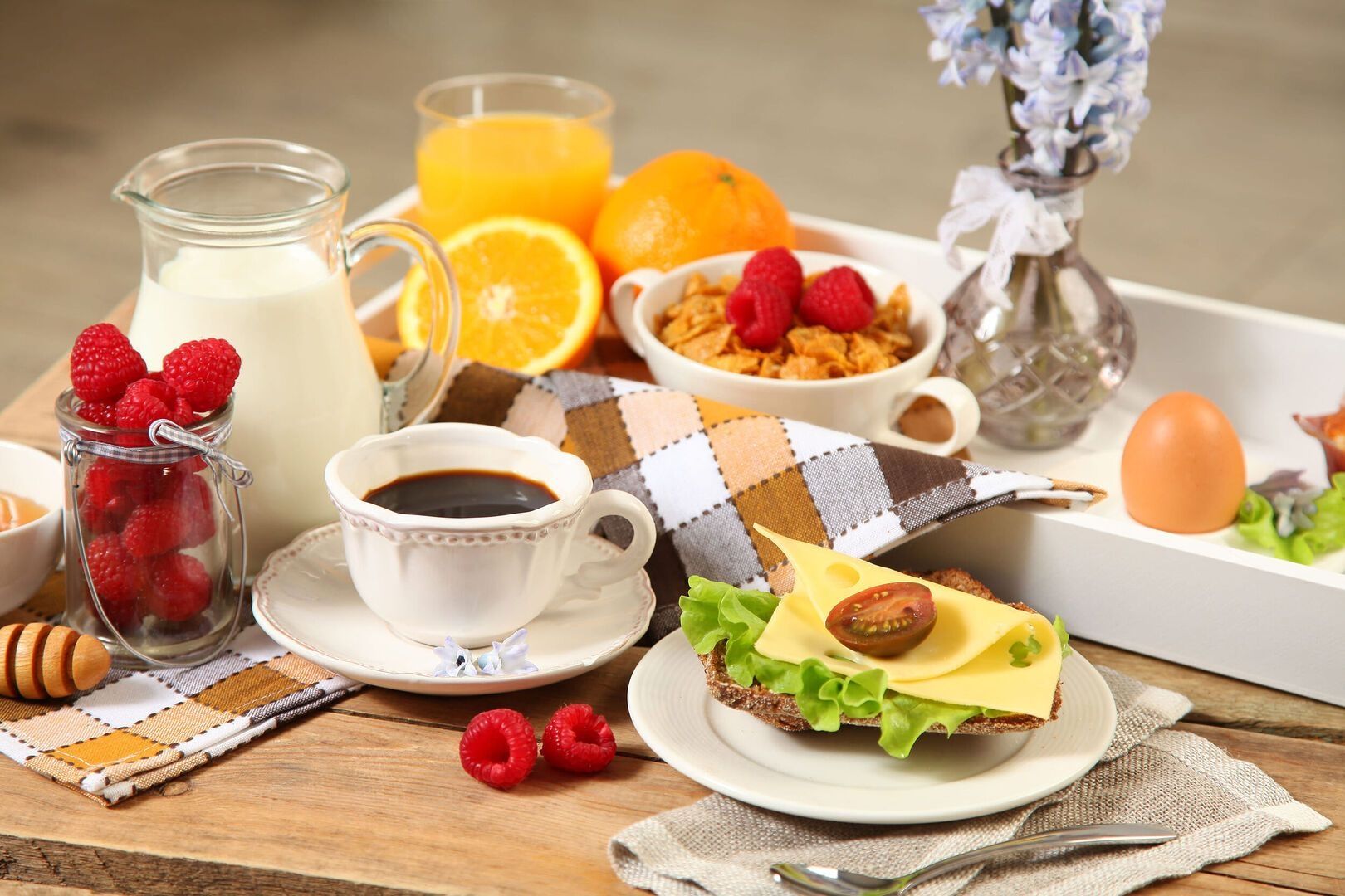 Frühstückstablett mit Kaffee, Milch, Orangensaft, Brot mit Käse und Tomate, Cornflakes mit Beeren, gekochtem Ei und frischen Himbeeren.