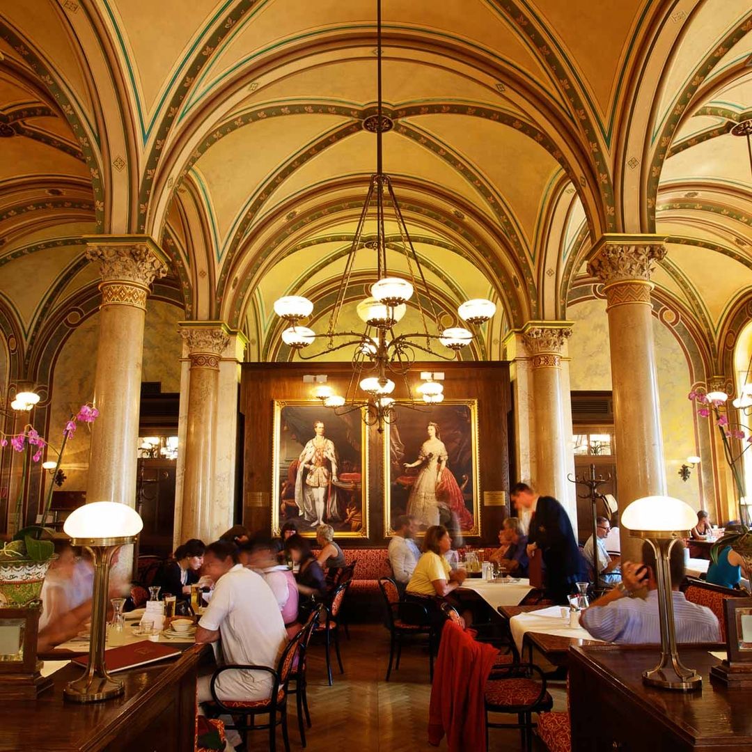 Innenansicht des Cafés Central mit hohen Decken kunstvollen Säulen und Gemälden im Hintergrund Gäste an den Tischen