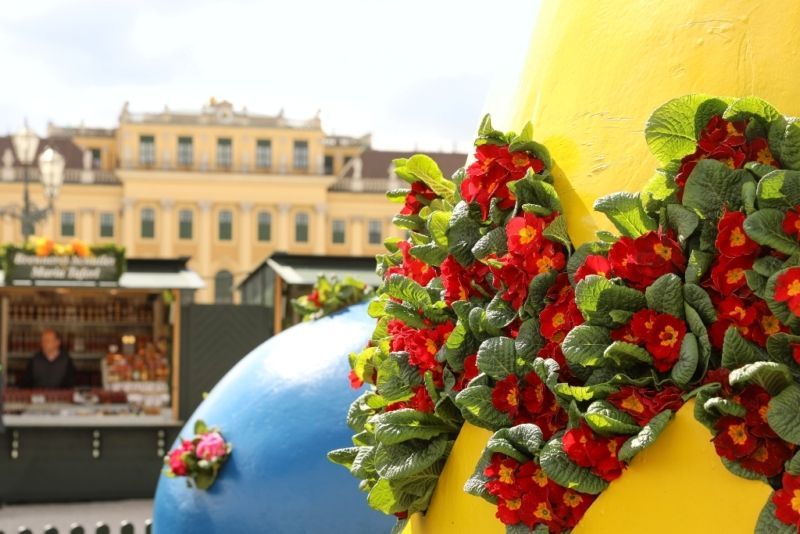 Detailaufnahme von einem Osterstand mit einer großen Osterei Skulptur die mit roten Blumen geschmückt ist im Hintergrund Schloss Schönbrunn