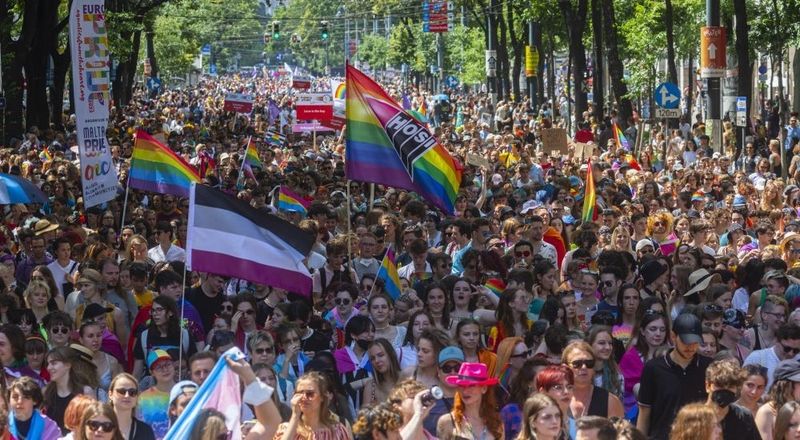 Grosse Menschenmenge auf einer Pride Parade mit Regenbogenflaggen.