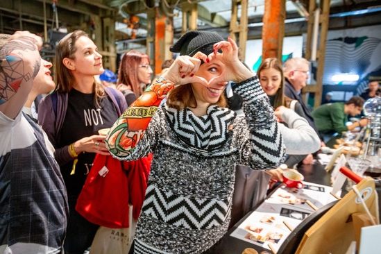 Lachende junge Frau hält die Hände in Herzform vor dem Gesicht und schaut hindurch.