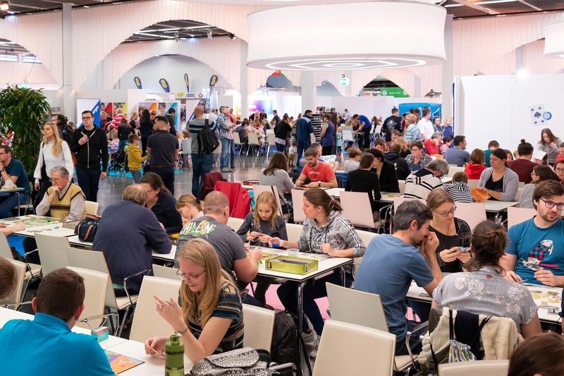 Viele Menschen in einer großen Halle sitzen an Tischen und spielen Gesellschaftsspiele