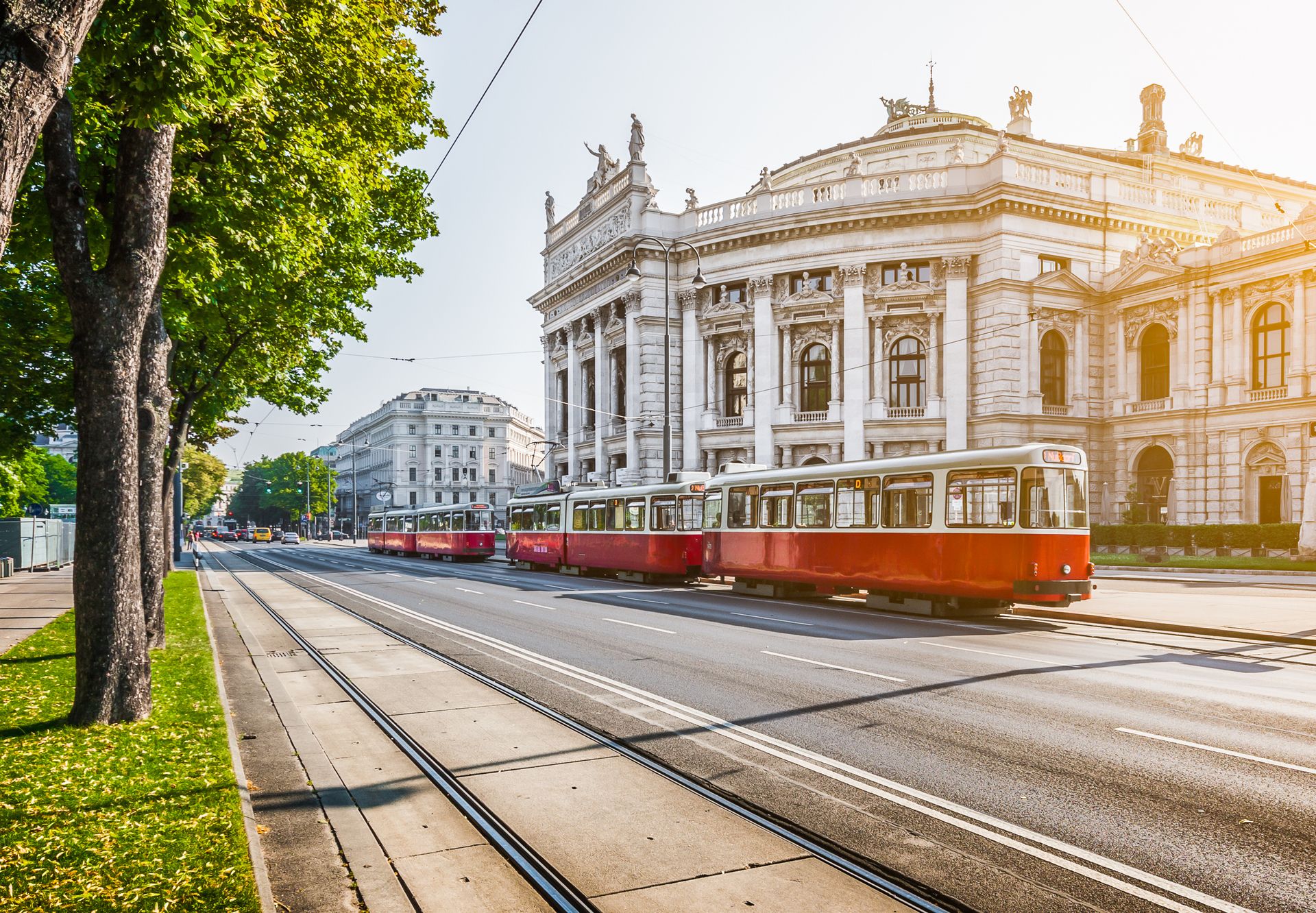 Rote Straßenbahn vor dem Burgtheater in Wien bei sonnigem Wetter auf der Ringstraße.