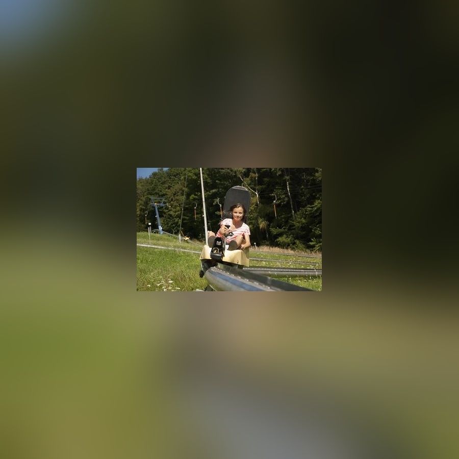 Lächelndes junges Mädchen fährt in einem Rodelschlitten auf einer Sommerrodelbahn.